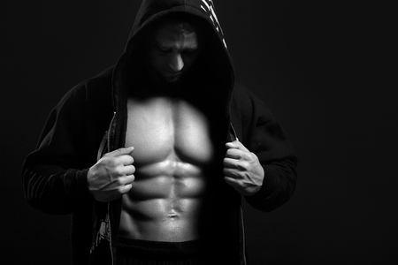 Man with muscular torso in hoodie on black showing his absの写真素材
