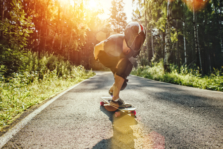Skater boy in helmet on longboard rides on road in beauty natureの写真素材