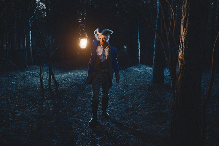 Man dressed as a courtier or officer 17-18 age go under night forest lighting his way with lanternの写真素材