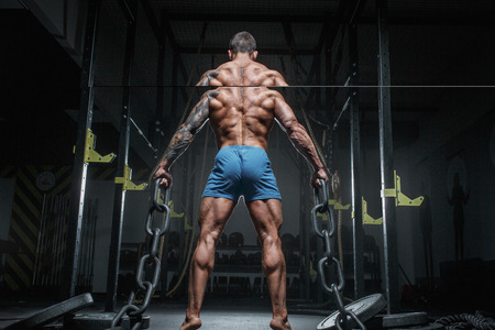 Athletic pumped man bodybuilder with chain in gym. Back view