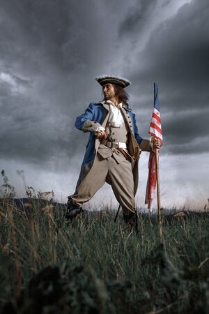 Man in United States War of Independence soldier costume with flag posing in forest. 4 july independence day of USA concept photo compositionの写真素材