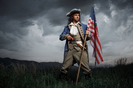 Man in United States War of Independence soldier costume with flag posing in forest. 4 july independence day of USA concept photo compositionの写真素材