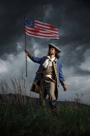American revolution war soldier with flag of colonies over dramatic landscape. 4 july independence day of USA concept photo composition: soldier and flag.の写真素材