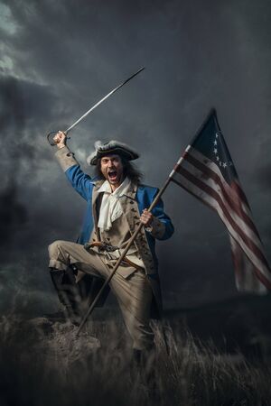 American revolution war soldier with flag of colonies and saber over dramatic landscape. 4 july...