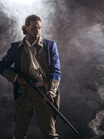 American revolution war soldier with flag of colonies and musket gun over dramatic smoke background. 4 July independence day of USA concept photo composition: soldier and flag.の写真素材
