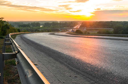 The road descending from the hill to the bridge in the early morning in summerの写真素材