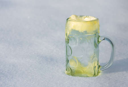 The large glass mug with beer foam frozen in the snowの写真素材