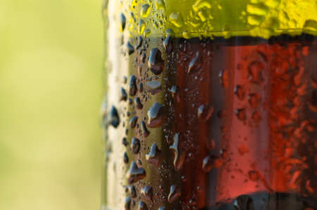 Droplets on the bottle of red wine in the summer against the backdrop of greeneryの写真素材