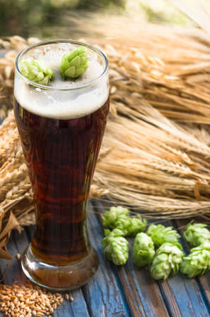 large glass of dark beer, malt, hops, barley ears standing on an old wooden table dyeing, natural backgroundの写真素材