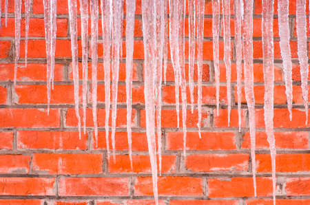 Icicles hanging against a background of red brick wallの写真素材