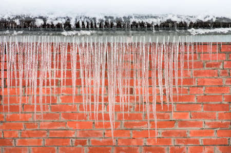Icicles hanging against a background of red brick wallの写真素材