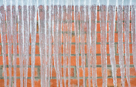 Icicles hanging against a background of red brick wallの写真素材