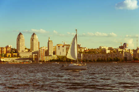 Towers twin on the river bank in the great Ukrainian city of the Dnipro and sailboat yacht, yellow retro toning, backgroundの写真素材