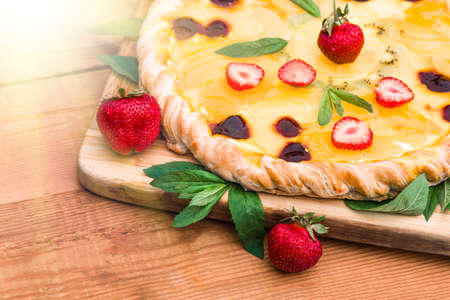 Fruit pizza with strawberries, cherries, cream, jelly, pineapple, kiwi and mint leaves, lying on a wooden cutting board, home-made. dessert background, closeupの写真素材