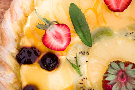 Fruit pizza with strawberries, cherries, cream, jelly, pineapple, kiwi and mint leaves, lying on a wooden cutting board, home-made. dessert background, closeupの写真素材