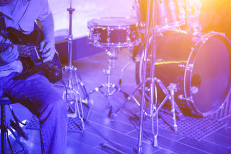 Man playing the guitar on stage against the background of the drum set illuminated in blue lightの写真素材