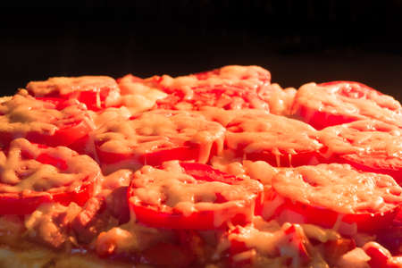 pizza with tomatoes and cheese closeup on a dark backgroundの写真素材