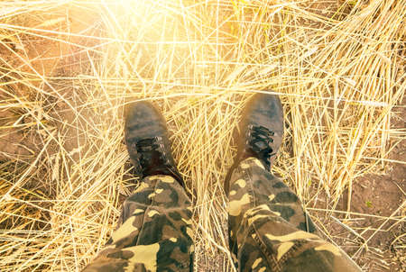 feet of a man in dirty shoes and camouflaged protective pants in wheat fieldの写真素材