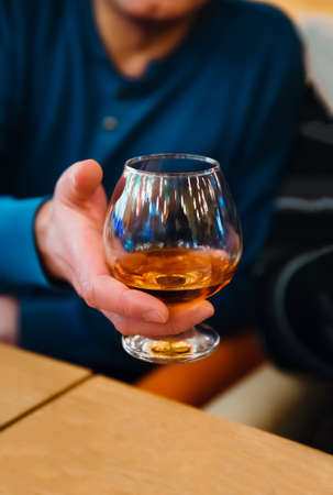 Man holding a glass of alcohol drink, man offers whiskey. A glass of whiskey in the hand of a man...