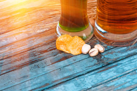 pistachios and potato chips lying on a painted old table near glasses of classic and Irish green beer, closeup, on St. Patrick's Dayの写真素材