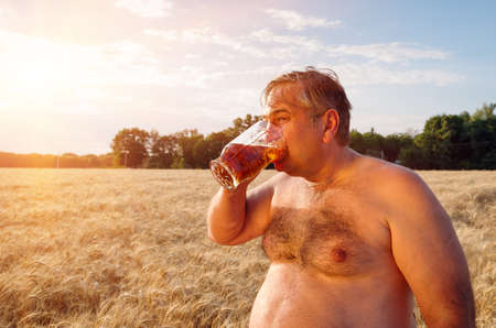 A fat man drinking beer in the field of barley