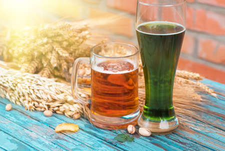 Green beer for St. Patrick's Day against the background of a ceramic wall stands on an old wooden colored table along with beer ingredients - shamrock , wheat, barley and snacks - pistachios, chipsの写真素材