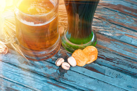 pistachios and potato chips lying on a painted old table near glasses of classic and Irish green beer, closeup, on St. Patrick's Dayの写真素材