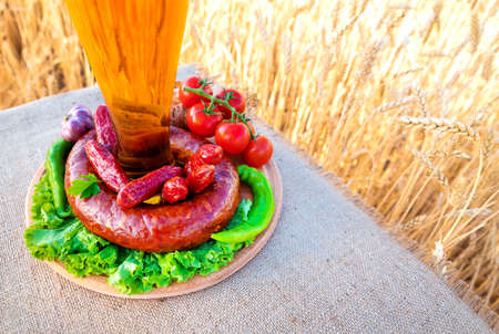 beer in a glass, sausage, vegetables on a table in a wheat fieldの写真素材