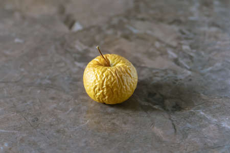 Wrinkled yellow old apple lies on the table top.