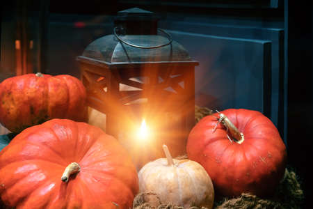 Old lantern with burning candle, pumpkins and autumn decorations in a dark room.