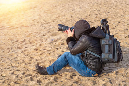 Photographer traveler with a camera and a backpack on the beach in spring when it is still cold, takes pictures .の写真素材