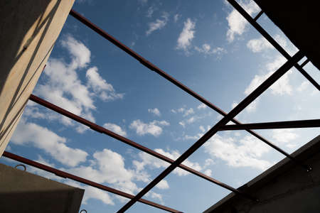 Silhouettes of roof beam in construction building look up in the blue sky.
