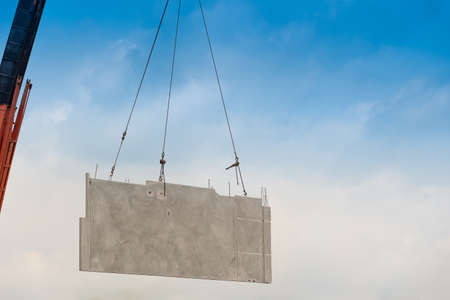 Construction site crane is lifting a precast concrete wall panel to installation building.の写真素材
