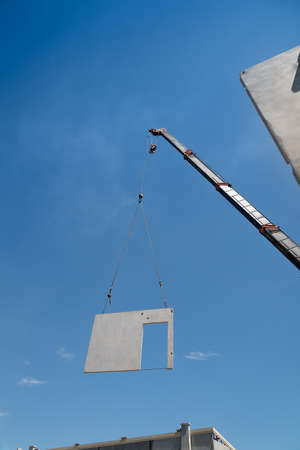 Construction site crane is lifting a precast concrete wall panel to installation building.の写真素材