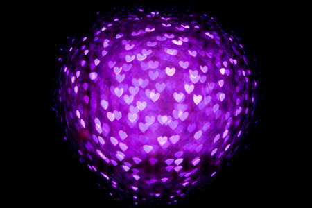 Blurred background with purple light bokeh in heart shape on black background.