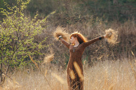 Young redhead woman walking in golden dried grass fieldの写真素材