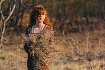 Young redhead woman walking in golden dried grass fieldの写真素材