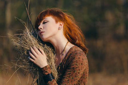Young redhead woman walking in golden dried grass fieldの写真素材