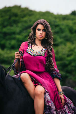 Beautiful gypsy in violet dress with a black horseの写真素材