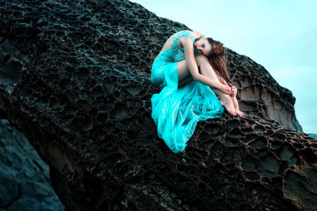 Fashionable woman posing on a beach with rocks in a long dressの写真素材