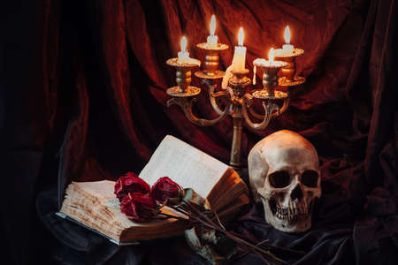 Still life with skull, dry roses, antique book and candlestick