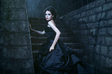 Attractive woman in black dress near stone wallの写真素材