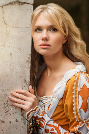 Beautiful blond woman in medieval dress walking near old building