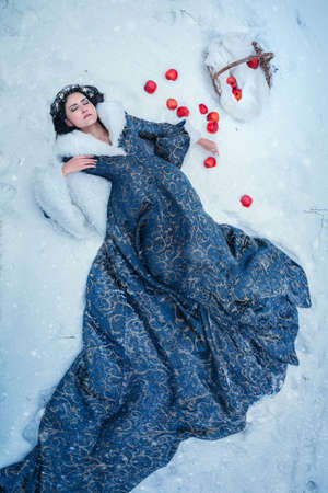 Portrait of young woman dressed in blue coat. She is walking in the winter forest holding a basket with applesの写真素材