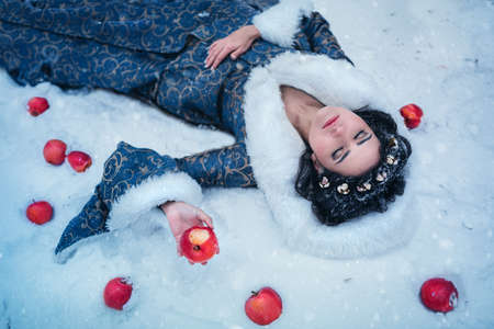 Portrait of young woman dressed in blue coat. She is walking in the winter forest holding a basket with applesの写真素材