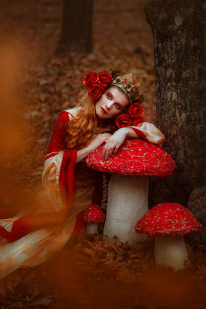 A young woman in red medieval dress walking in wonderlandの写真素材