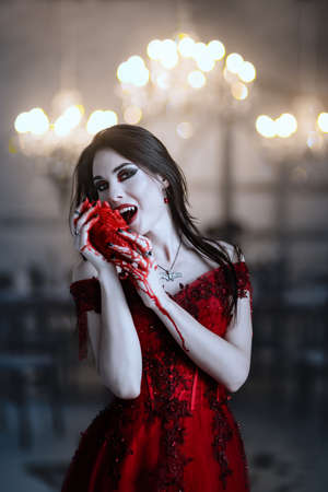 Bloodthirsty female vampire in red dress. Medieval interior