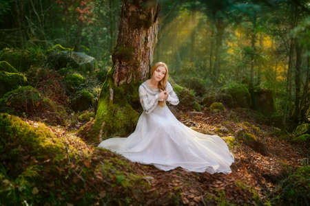 Beautiful young woman in a white dress in the middle of a forestの写真素材