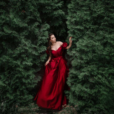 Beautiful woman in red dress walking in the garden full of roses.
