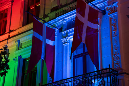 Two Danish flags hang on a building, illuminated by colorful lights at night, creating a vibrant and festive nighttime scene.の写真素材